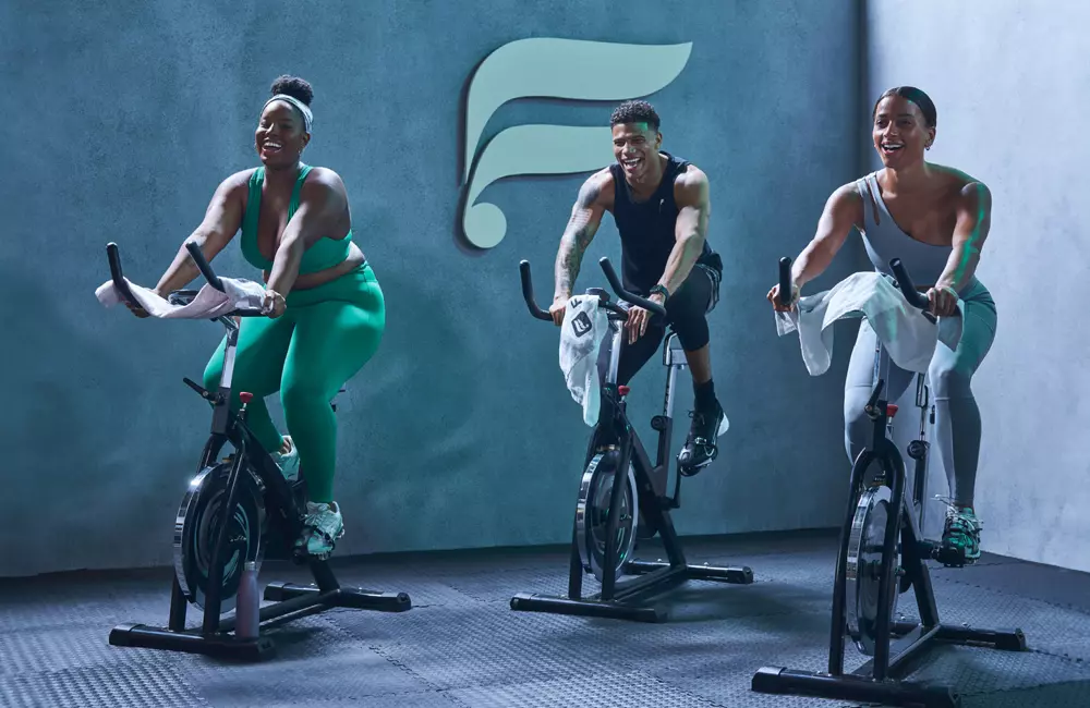 drei lächelnde Menschen beim trainieren auf einem Spinning-Bike