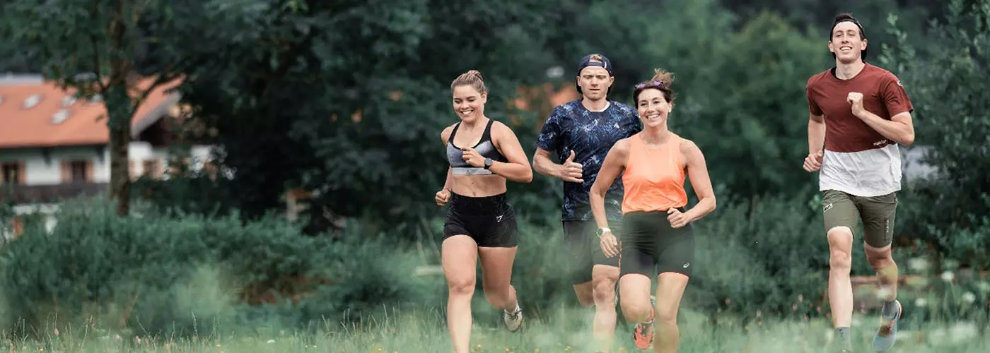 vier fröhliche Menschen joggen gemeinsam durch eine grüne Landschaft