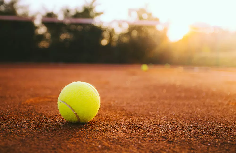Tennisball liegt auf Tennisplatz, im Hintergrund Sonnenuntergang