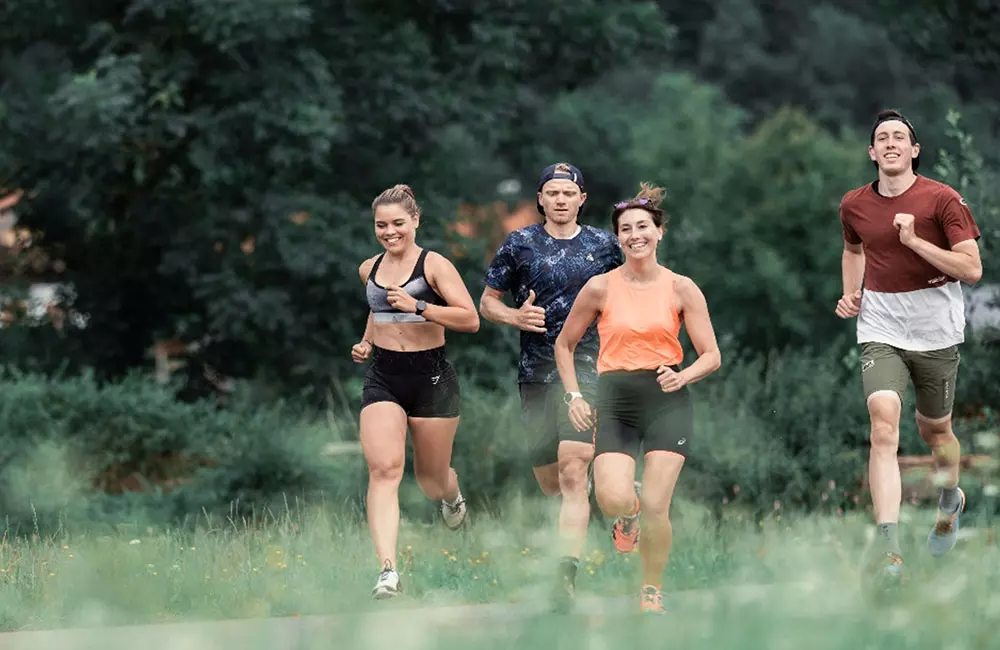 vier fröhliche Menschen joggen gemeinsam durch eine grüne Landschaft