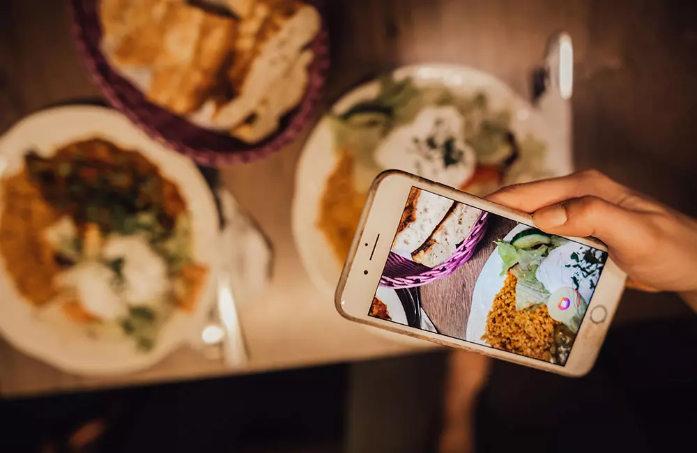 Frau macht mit Smartphone ein Foto von appetitlich aussehenden Essen