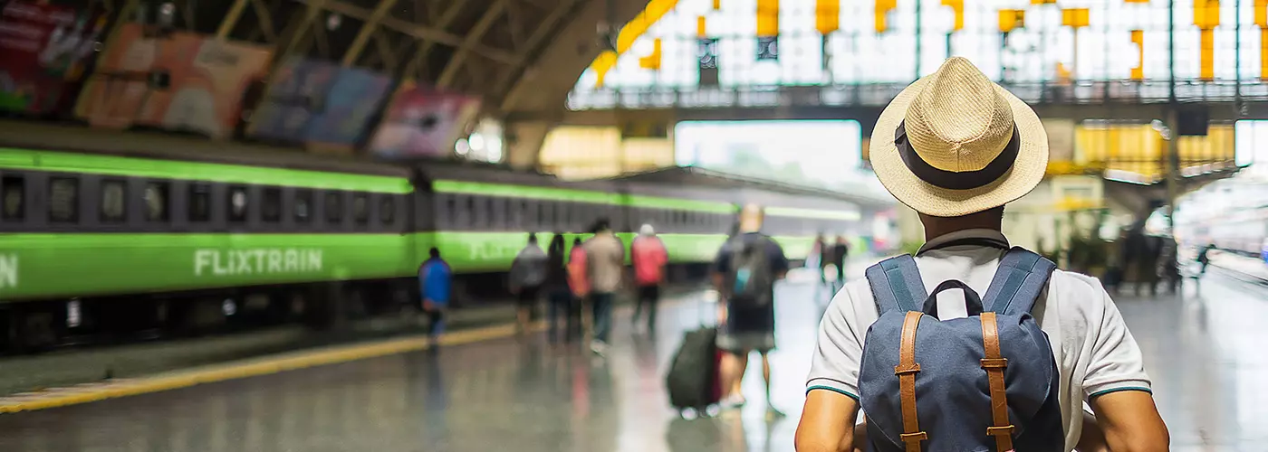 Mann mit rucksack und Strohhut steht im Bahnhof und schaut auf Flixtrain-Zug