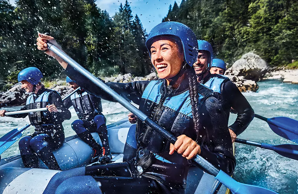 junge lächelnde Menschen bei Wildwasser-Rafting im Bergfluss umgeben von Wald