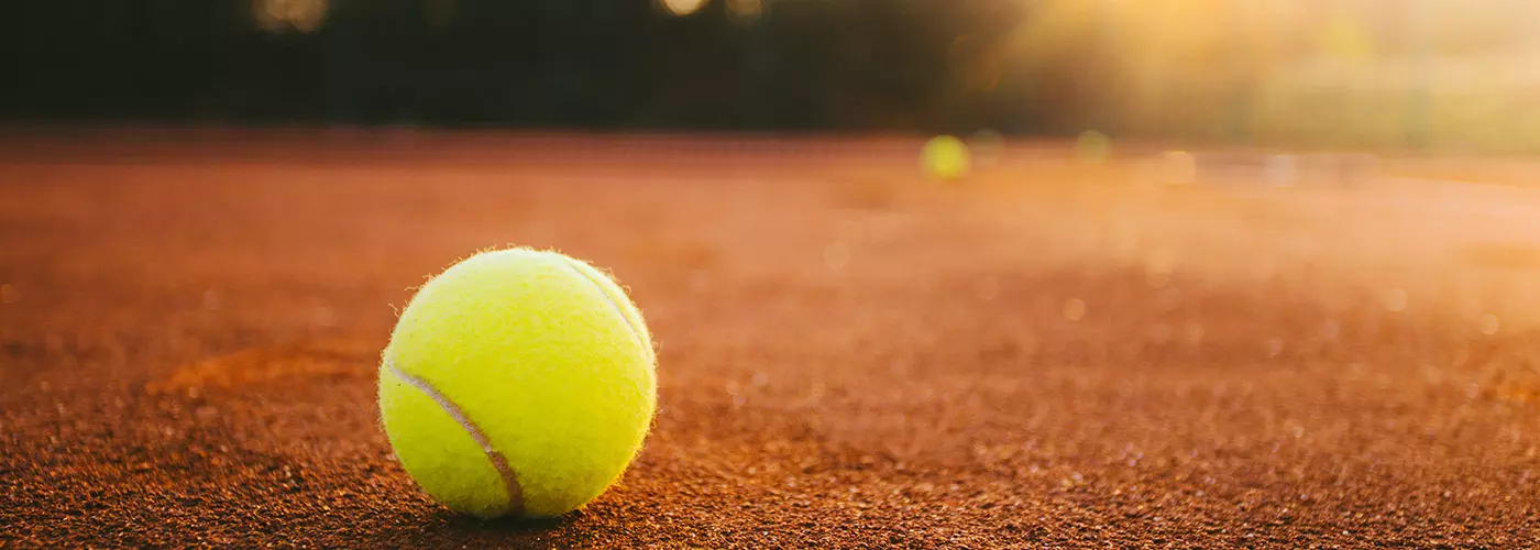 Tennisball liegt auf Tennisplatz, im Hintergrund Sonnenuntergang